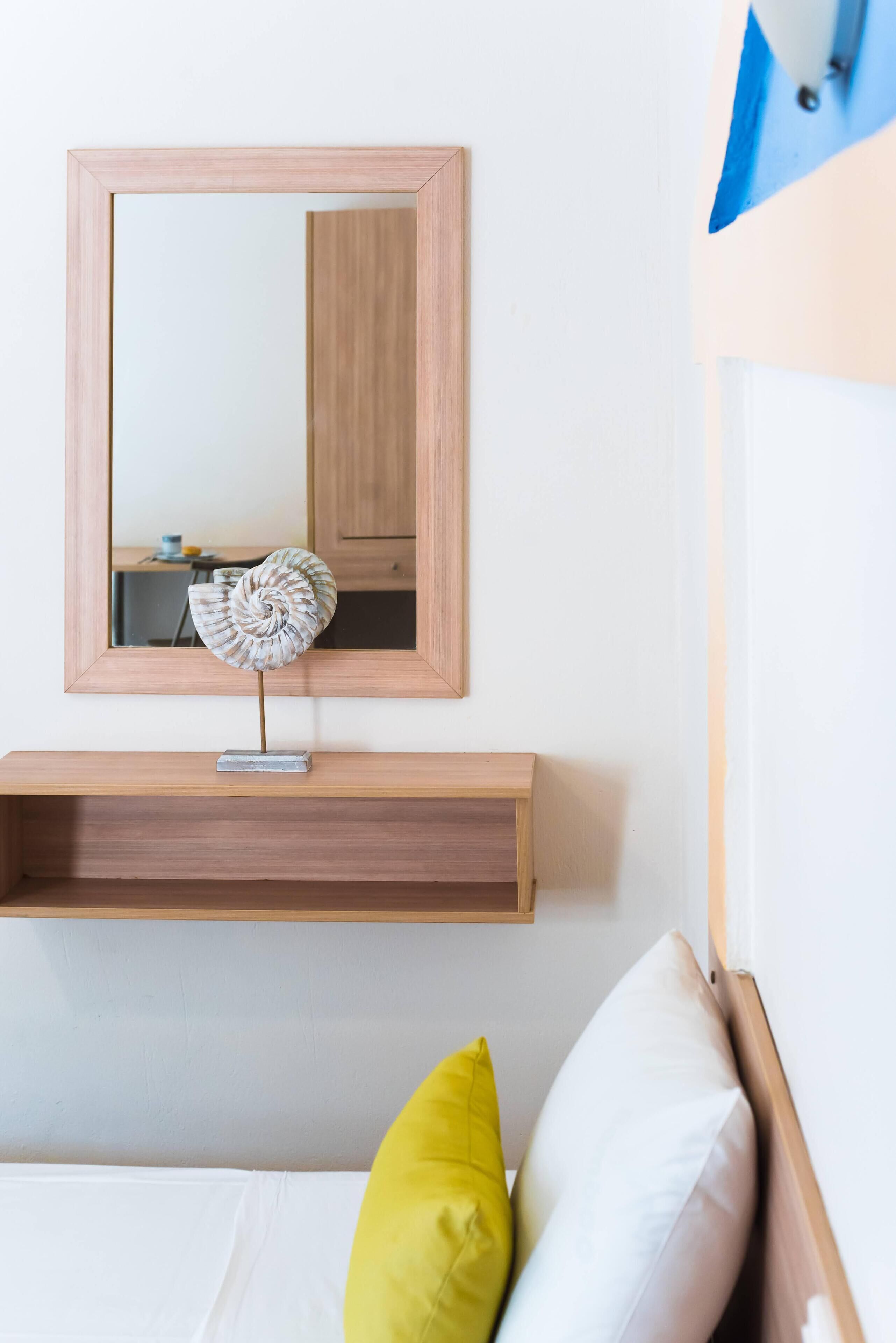 Un dormitorio con cabecera de madera, una mesita de noche con una pequeña escultura y un espejo encima.
