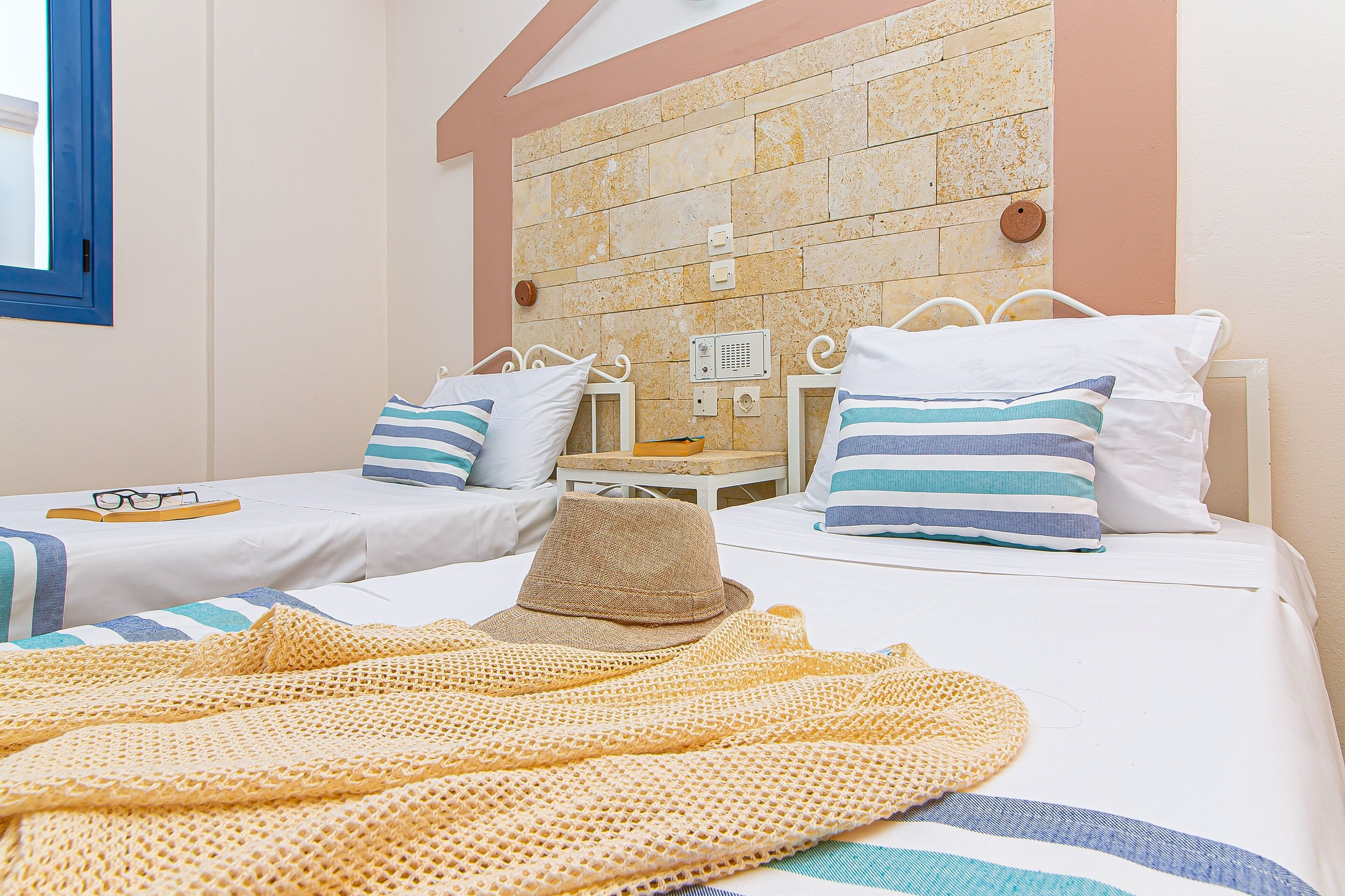 Una habitación de hotel con dos camas, cada una con ropa de cama a rayas y un sombrero sobre una de ellas.