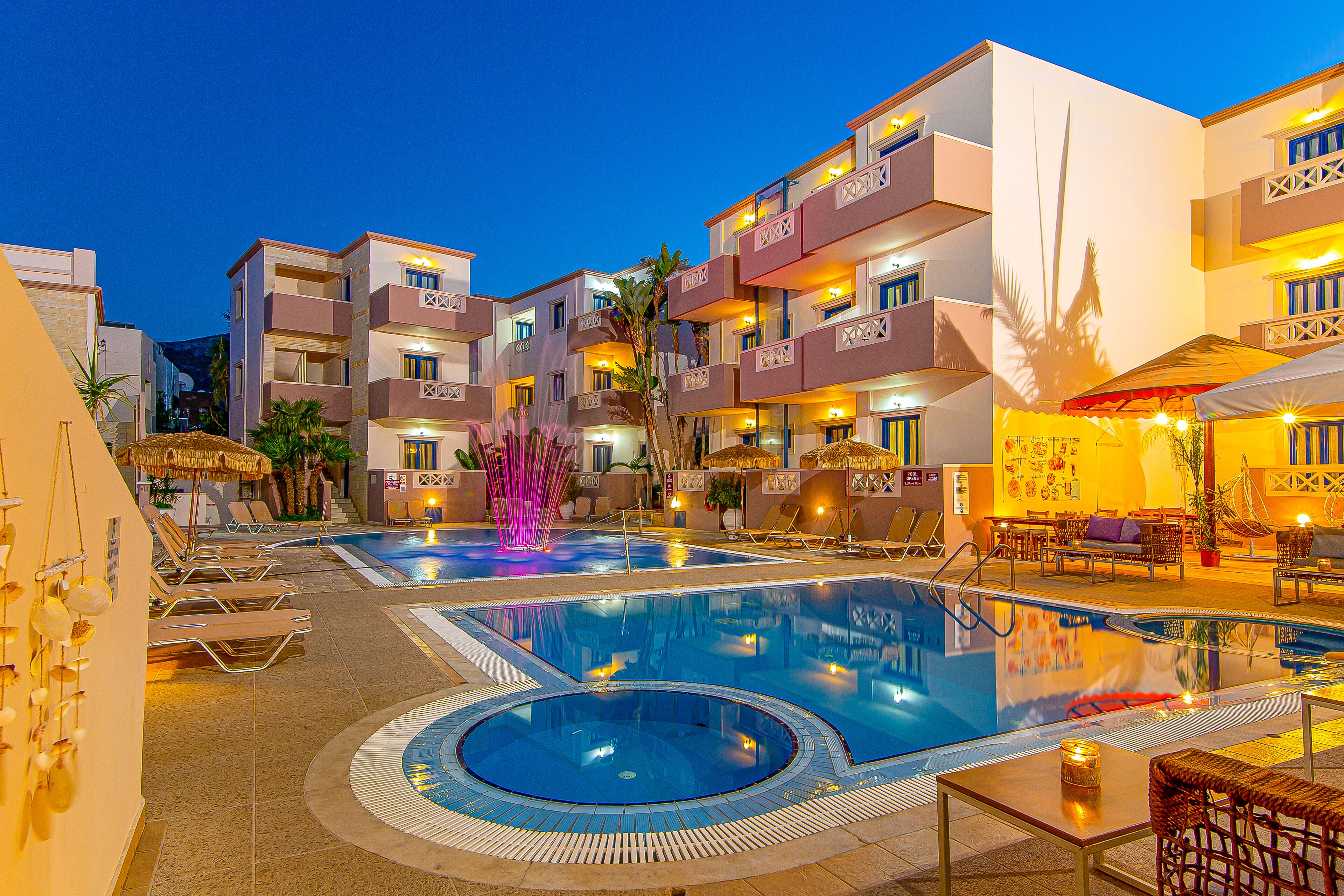A hotel pool area with multiple swimming pools, lounge chairs, and a decorative fountain.