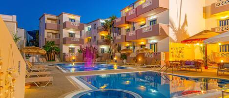 A hotel pool area with multiple swimming pools, lounge chairs, and a decorative fountain.