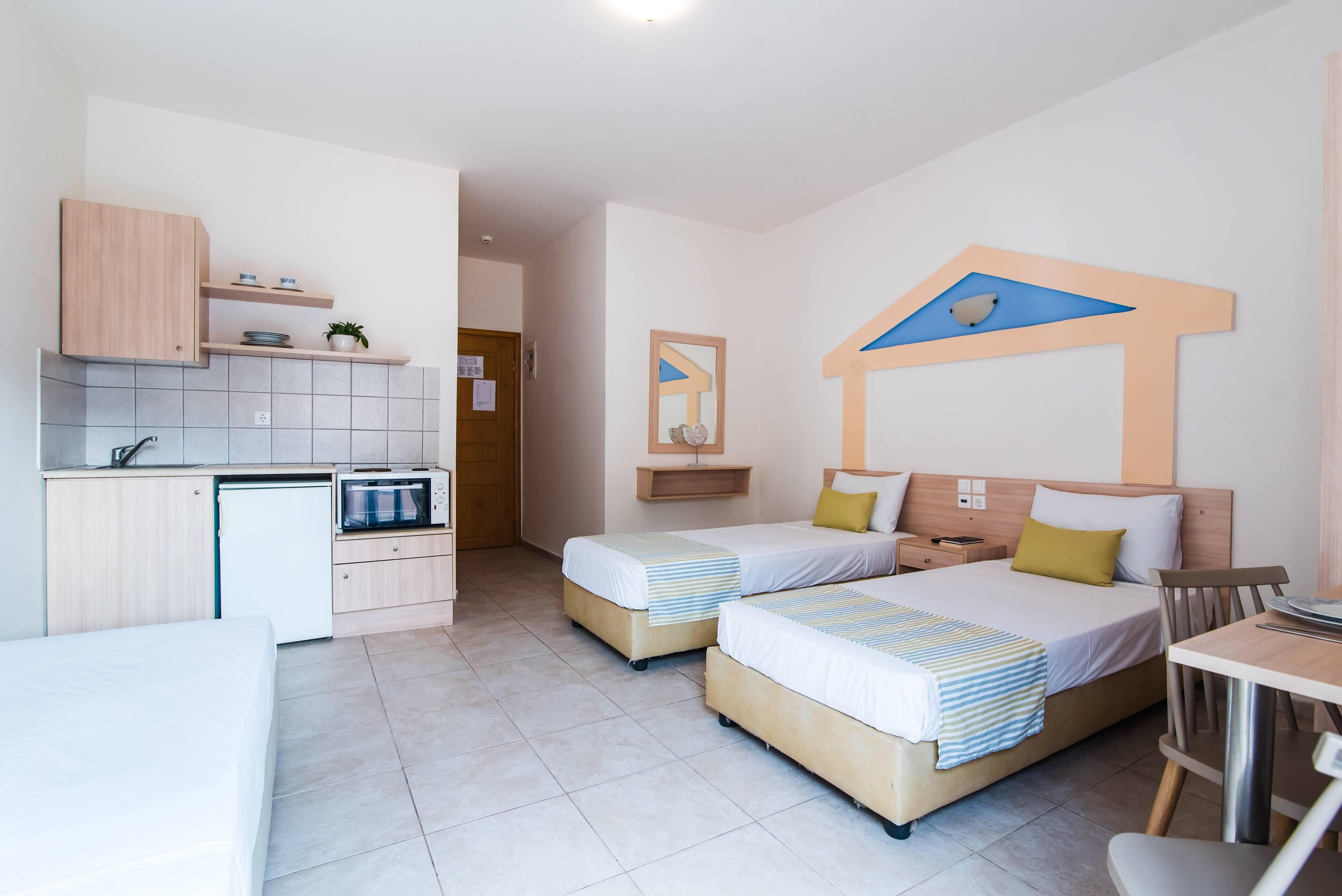 A compact hotel room with a kitchenette, two beds, a small dining area, and a bathroom.
