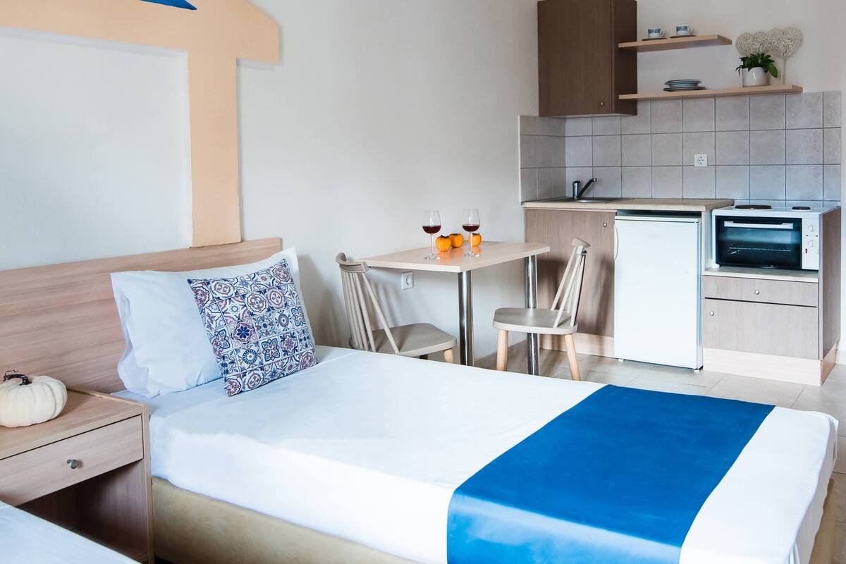 A hotel room with a bed, bedside table, a small kitchenette with a refrigerator, a microwave, and a sink.