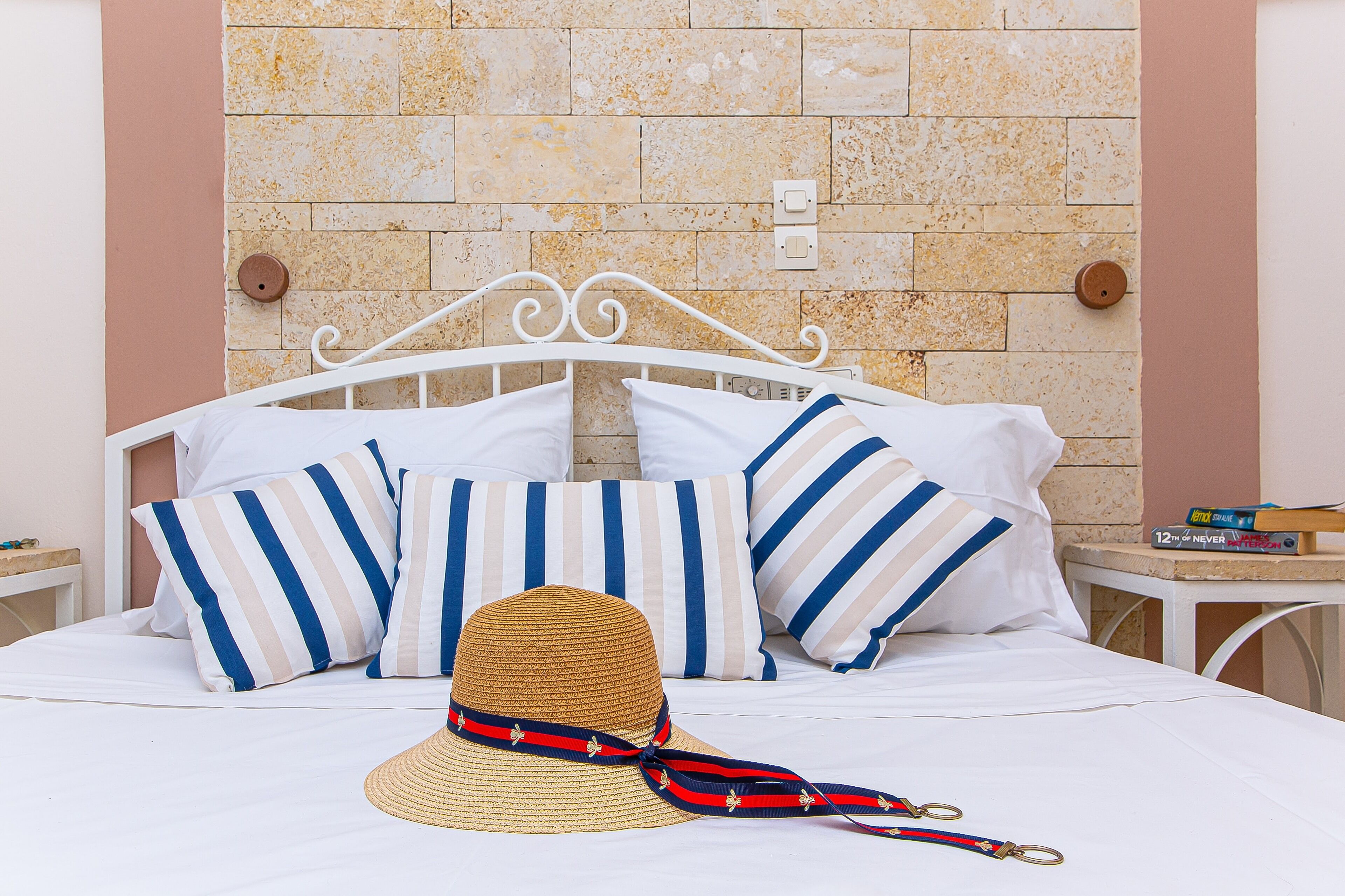 A bed with striped pillows, a straw hat, and a book on a nightstand.