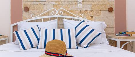 A bed with striped pillows, a straw hat, and a book on a nightstand.