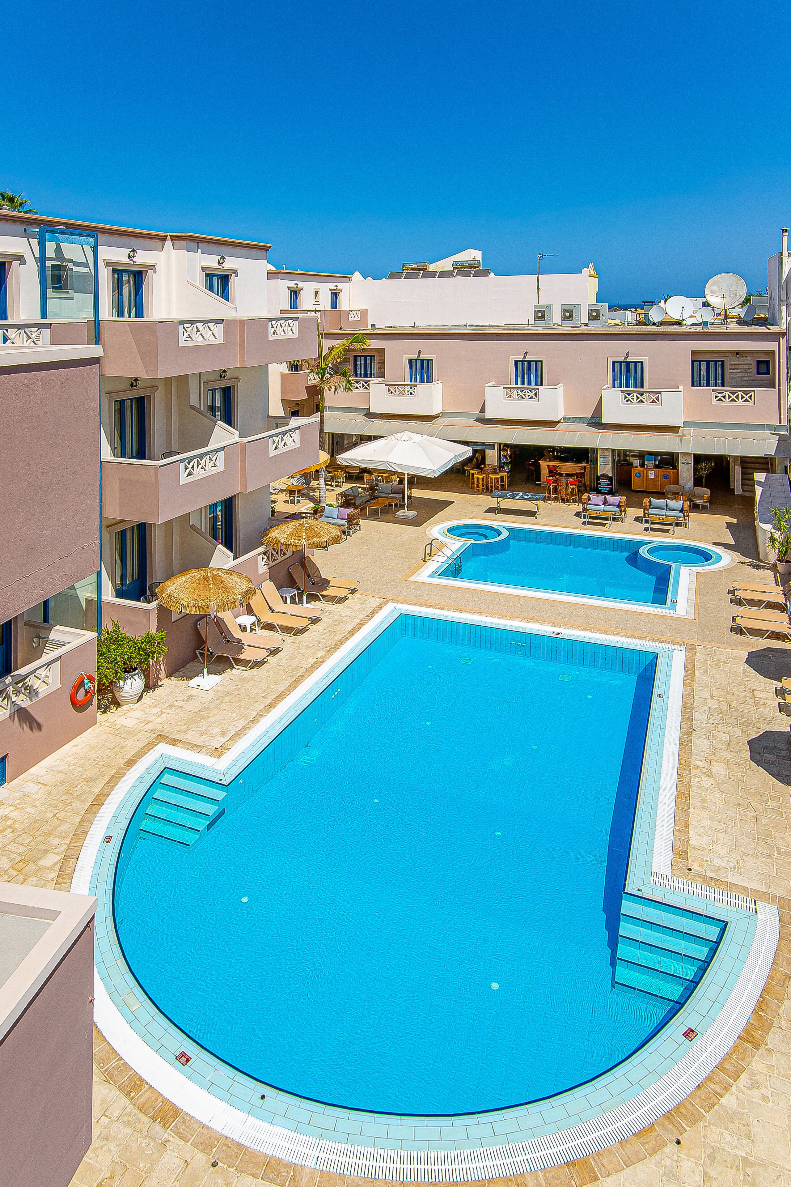 Un área de piscina en la azotea con dos piscinas, sillas de descanso, sombrillas y un bar.