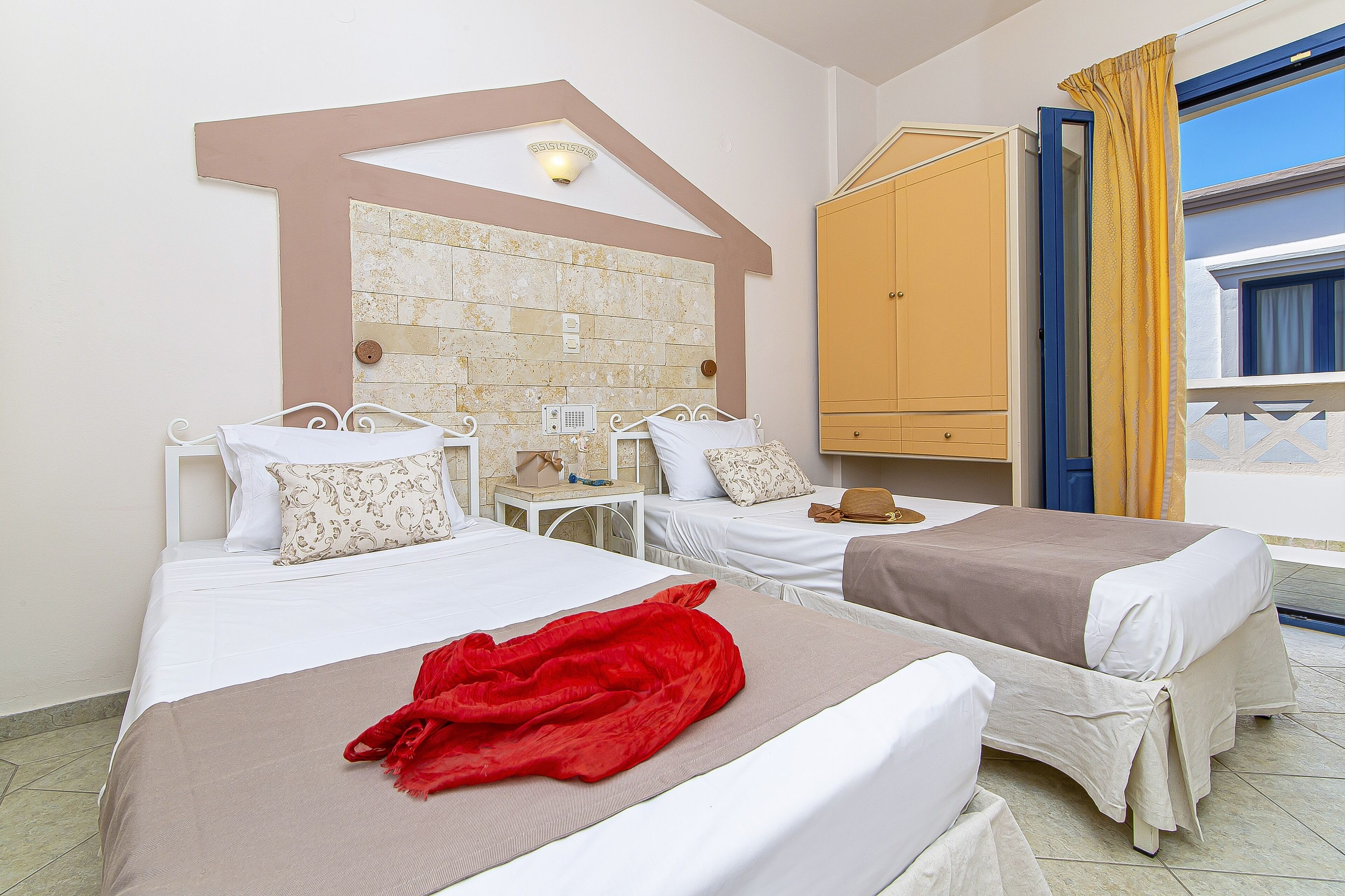 A hotel room with two beds, a wardrobe, a small table, and a window with curtains.