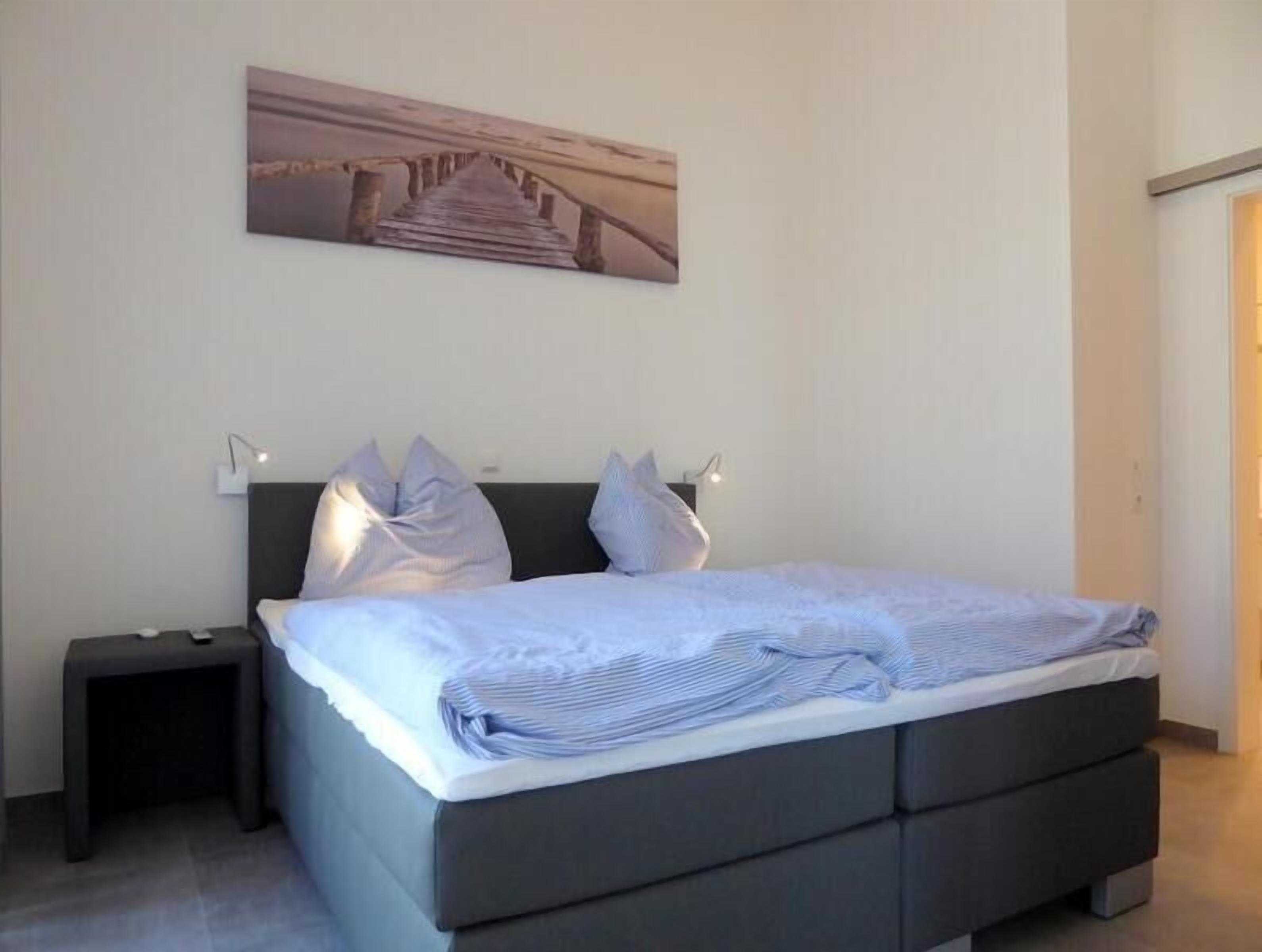 A modern bedroom with a bed, bedside tables, and a wall-mounted picture.
