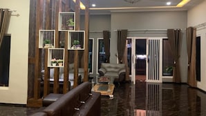 Een moderne woonkamer met een donkere marmeren vloer, een leren bank, een glazen salontafel en een houten decoratief paneel met ingelijste foto's.