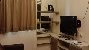 A compact living space with a flat-screen TV, a small desk, and a couch. - The Suites Metro Apartment by NFO Property (Bandung)