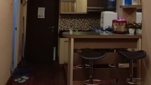 A narrow kitchen with a dark door, a small bar area with stools, and a tiled backsplash. - The Suites Metro Apartment by NFO Property (Bandung)