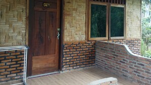Uma porta de madeira com placa de número, uma janela com padrão trançado e uma parede de tijolos.