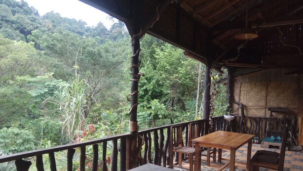 Mesa e cadeiras de madeira numa varanda com vista para uma área arborizada.