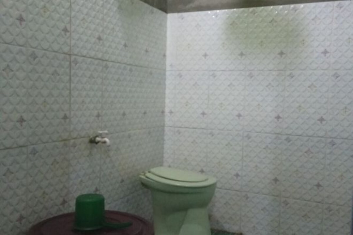 A bathroom with a toilet and a green container on the floor.