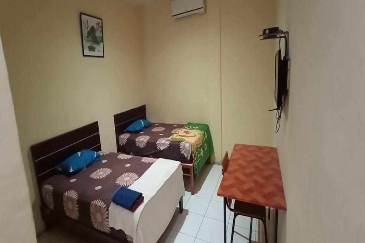 A small, clean room with two beds, a table, and a wall-mounted TV.
