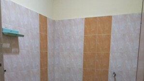 A small bathroom with a toilet, a shower area, and a trash bin.