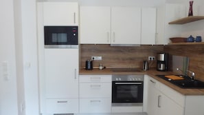 Eine moderne Küche mit weißen Schränken, einem eingebauten Backofen, einer Mikrowelle und einer Kaffeemaschine.