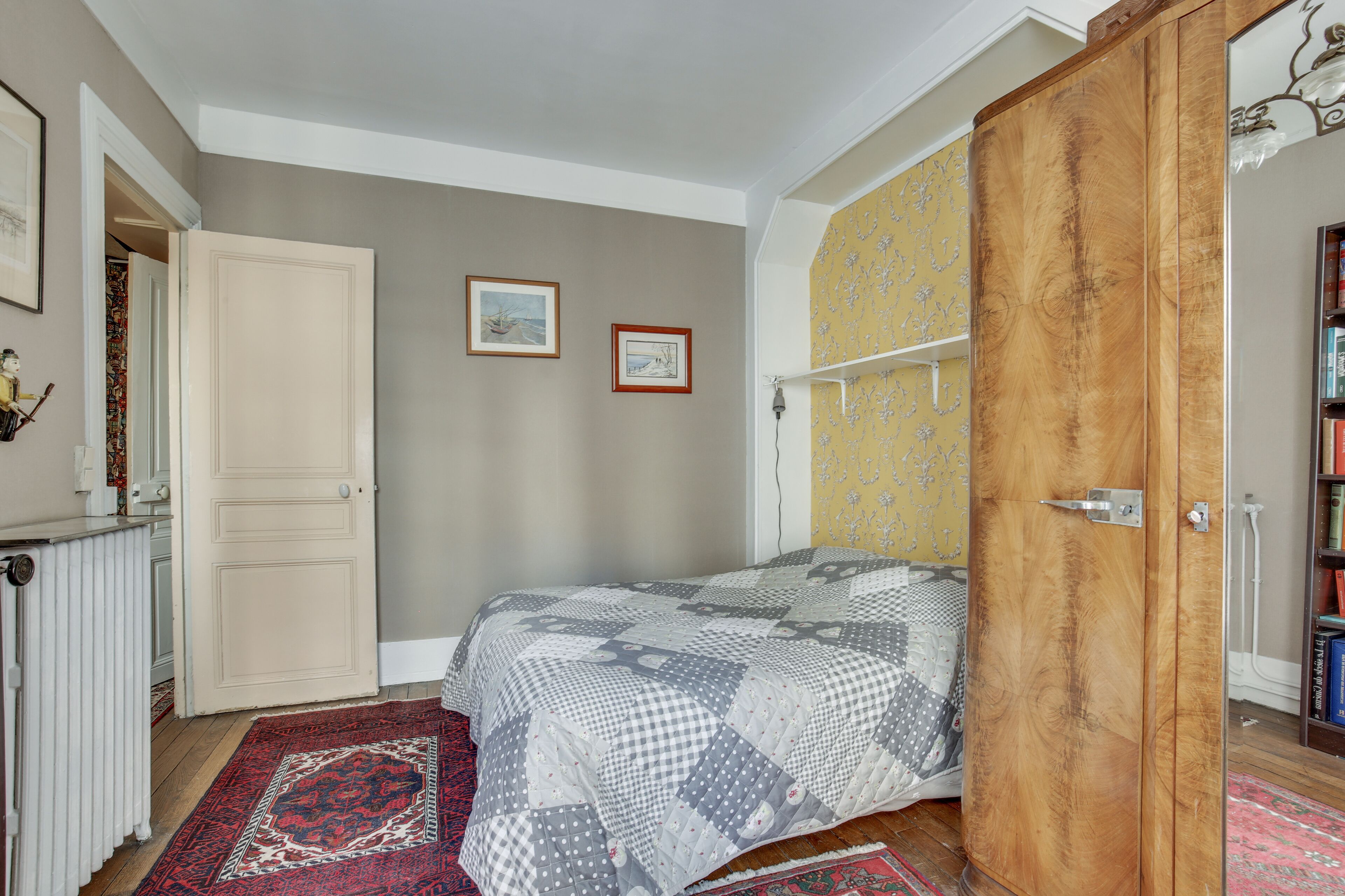 A bedroom with a bed, a wardrobe, a radiator, and a bookshelf.
