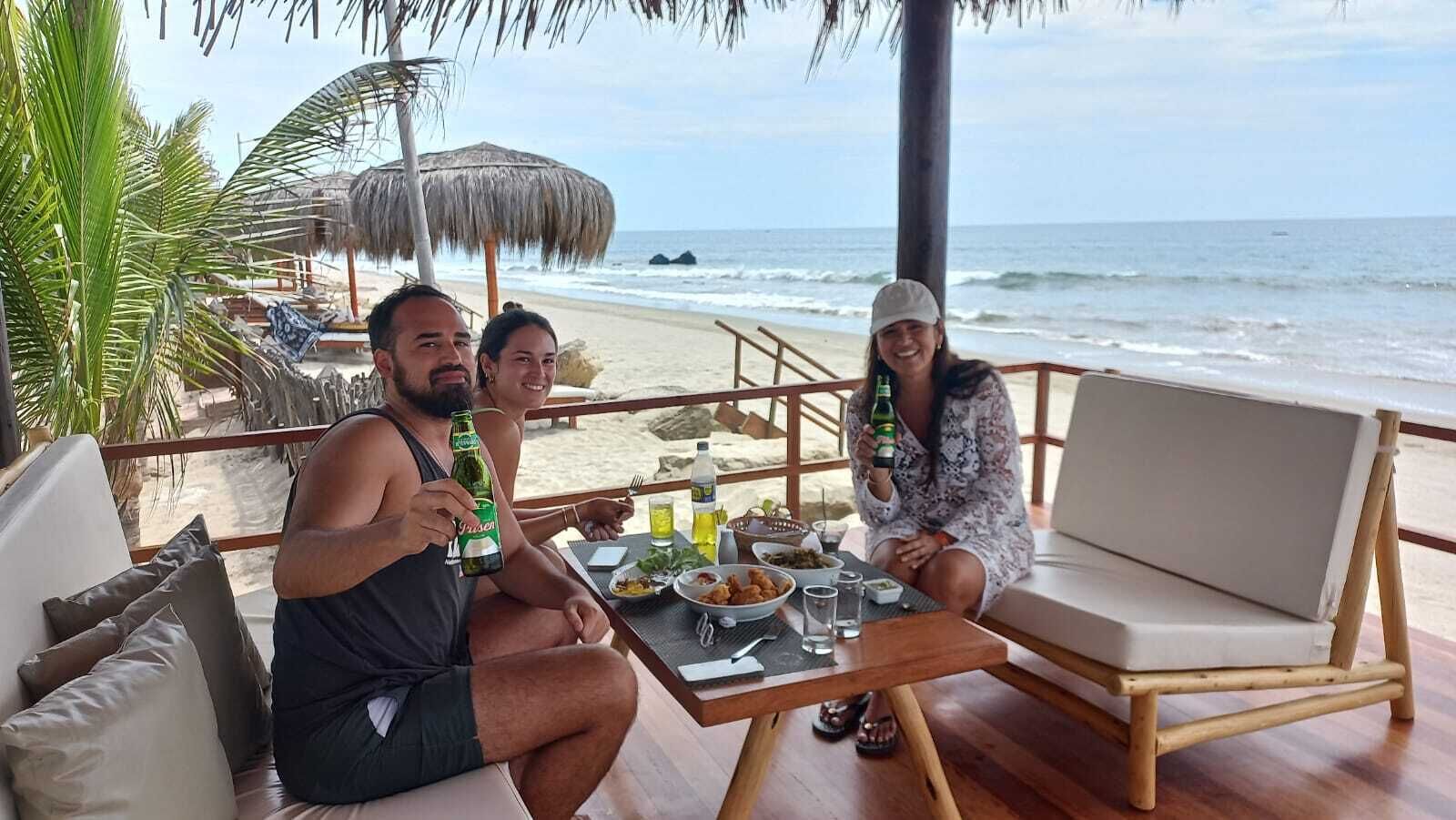 Um casal jantando em uma mesa de madeira com vista para a praia e o oceano.