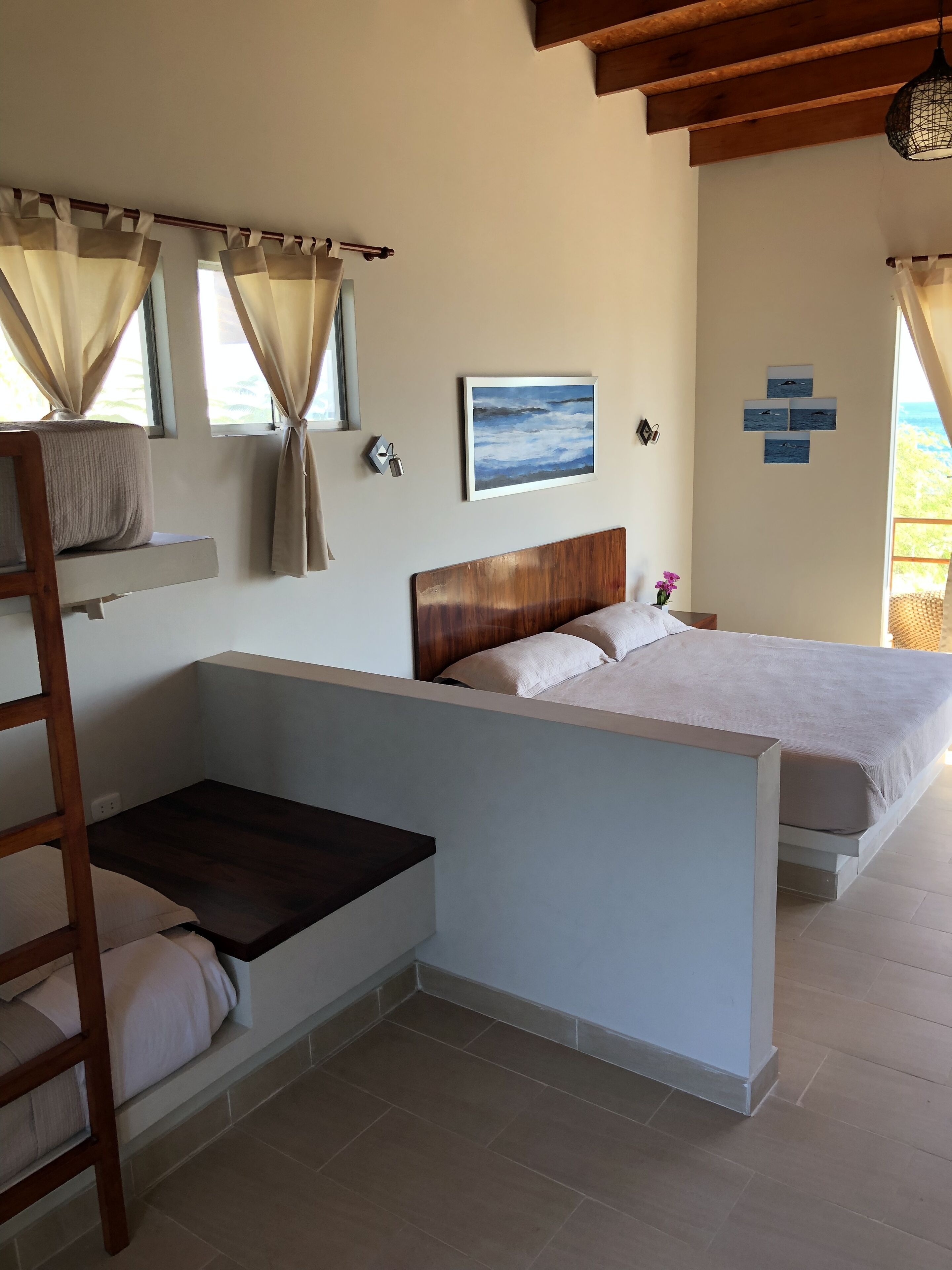 A bedroom with a bunk bed, a wooden headboard, a bedside table, and a window with curtains.