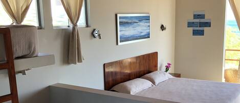 A bedroom with a bunk bed, a wooden headboard, a bedside table, and a window with curtains.