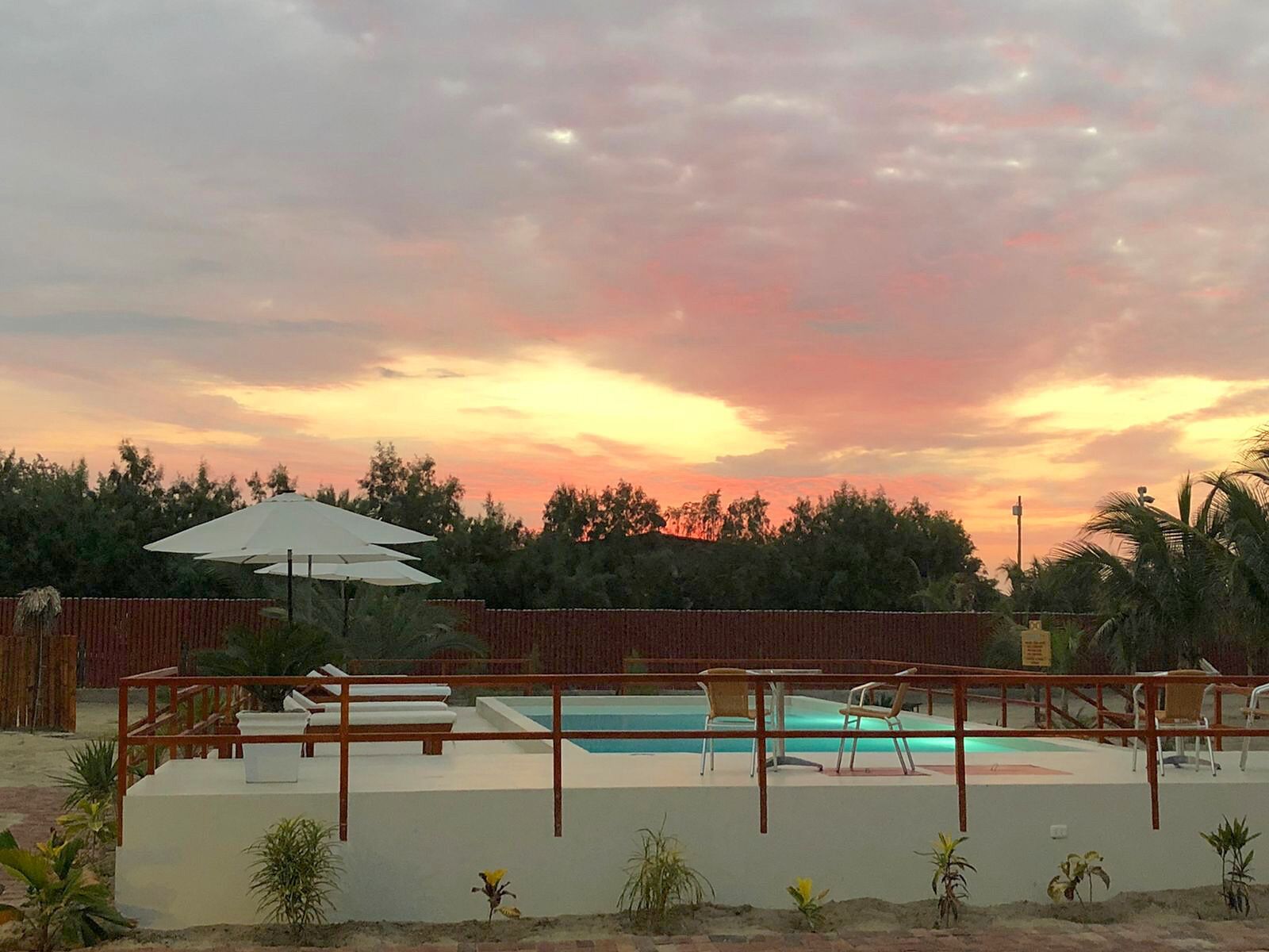 Un área de piscina con terraza de madera, sillas de descanso y una sombrilla blanca.