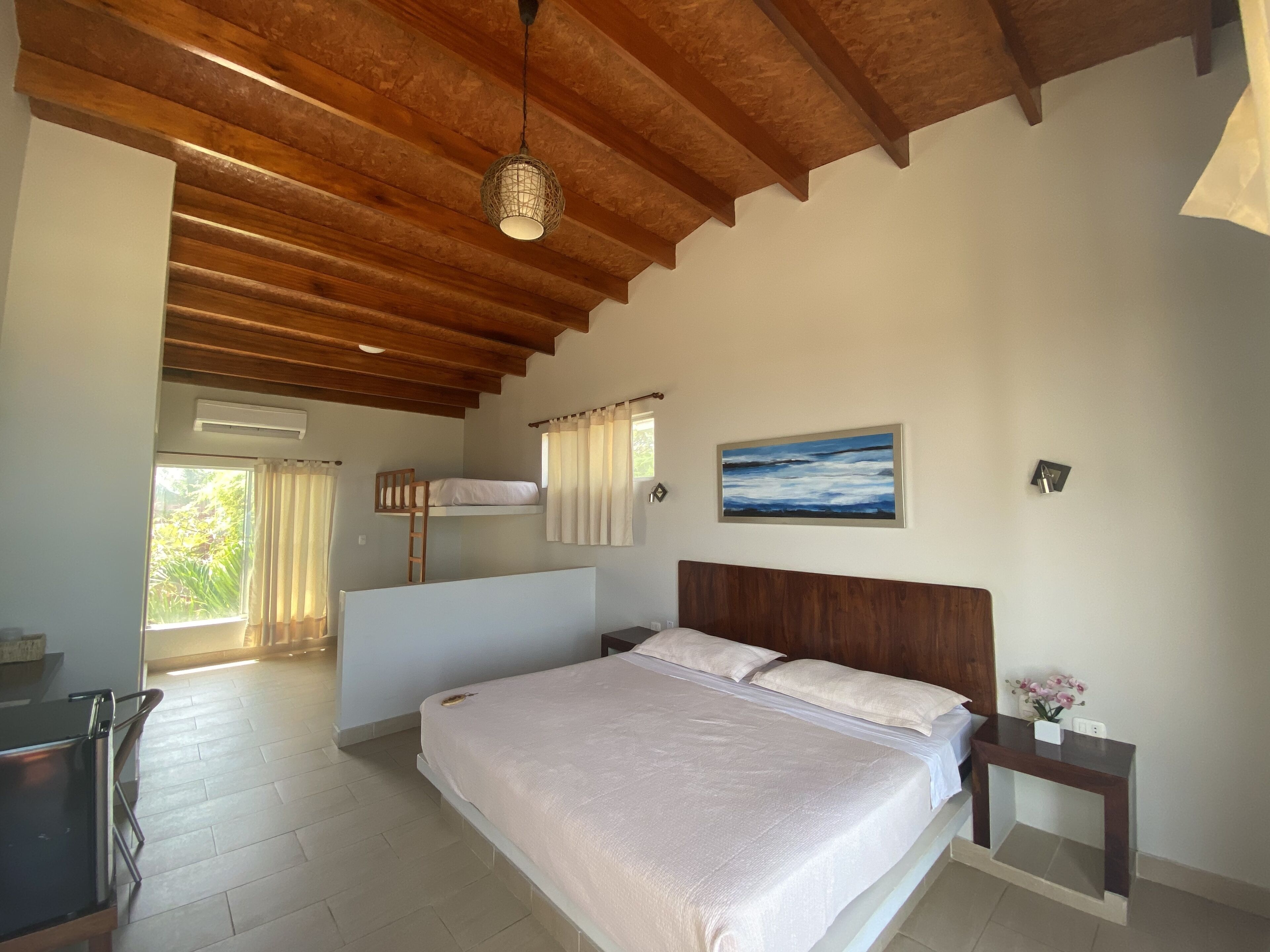 A bedroom with a bunk bed, a wooden ceiling, a bedside table, and a painting on the wall.