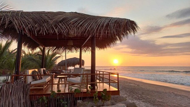 A beachside lounge with a thatched roof, wooden deck, and seating area overlooking the ocean at sunset. - El Samay Hotel Boutique (Canoas de Punta Sal)