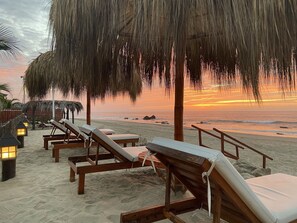 A beachside lounge area with wooden lounge chairs and thatched umbrellas, overlooking the ocean. - El Samay Hotel Boutique (Canoas de Punta Sal)