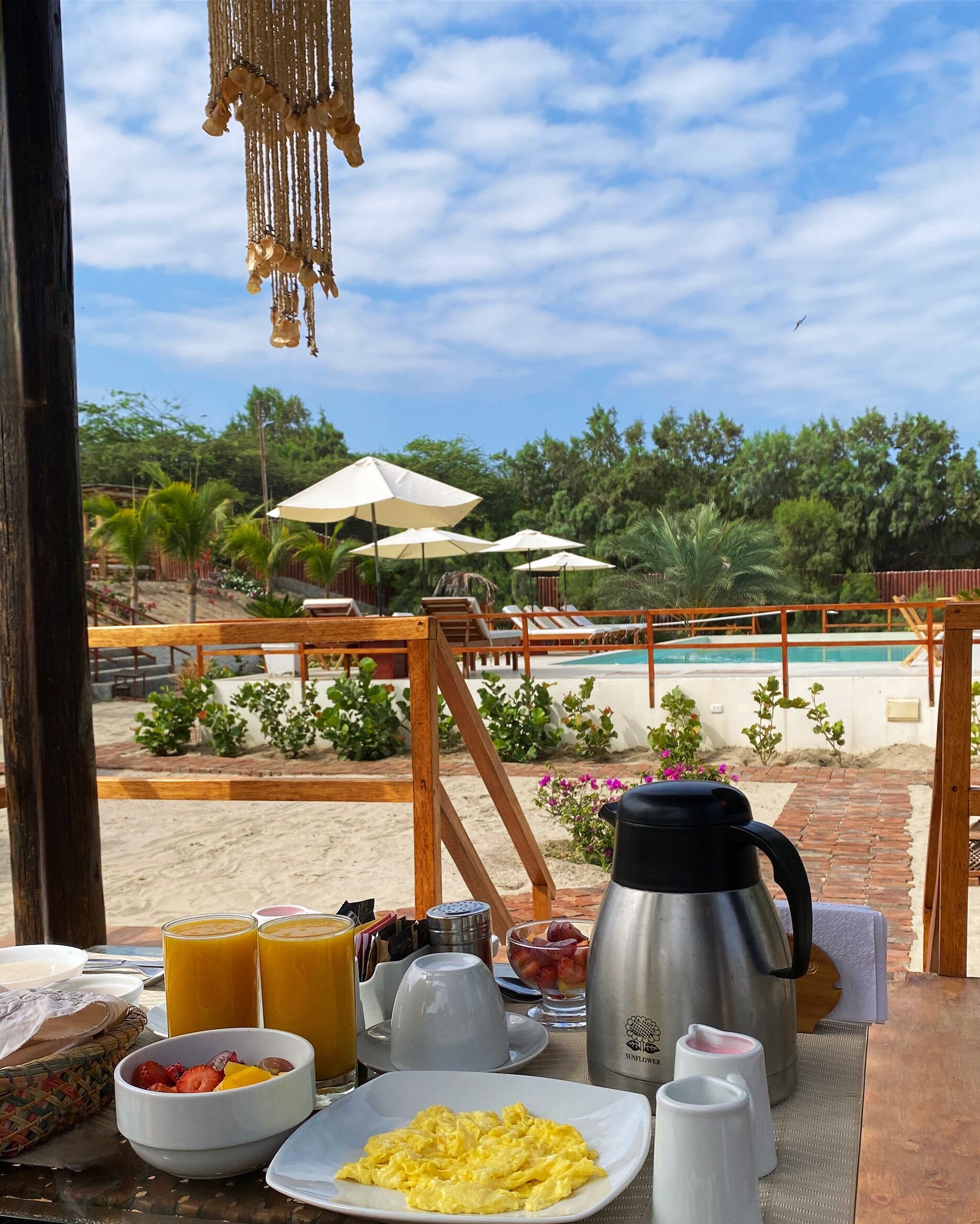 A breakfast setup with a pool view, including a table with breakfast items, a coffee pot, and umbrellas.