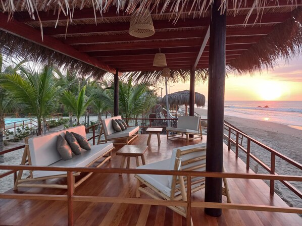A wooden deck with lounge chairs and tables, overlooking a beach at sunset. - El Samay Hotel Boutique (Canoas de Punta Sal)