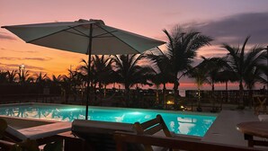A pool area with lounge chairs and umbrellas, surrounded by palm trees and a sunset view. - El Samay Hotel Boutique (Canoas de Punta Sal)