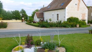 Ein Haus mit geneigtem Dach, ein kleiner Garten mit verschiedenen Pflanzen und eine Auffahrt mit Kies.