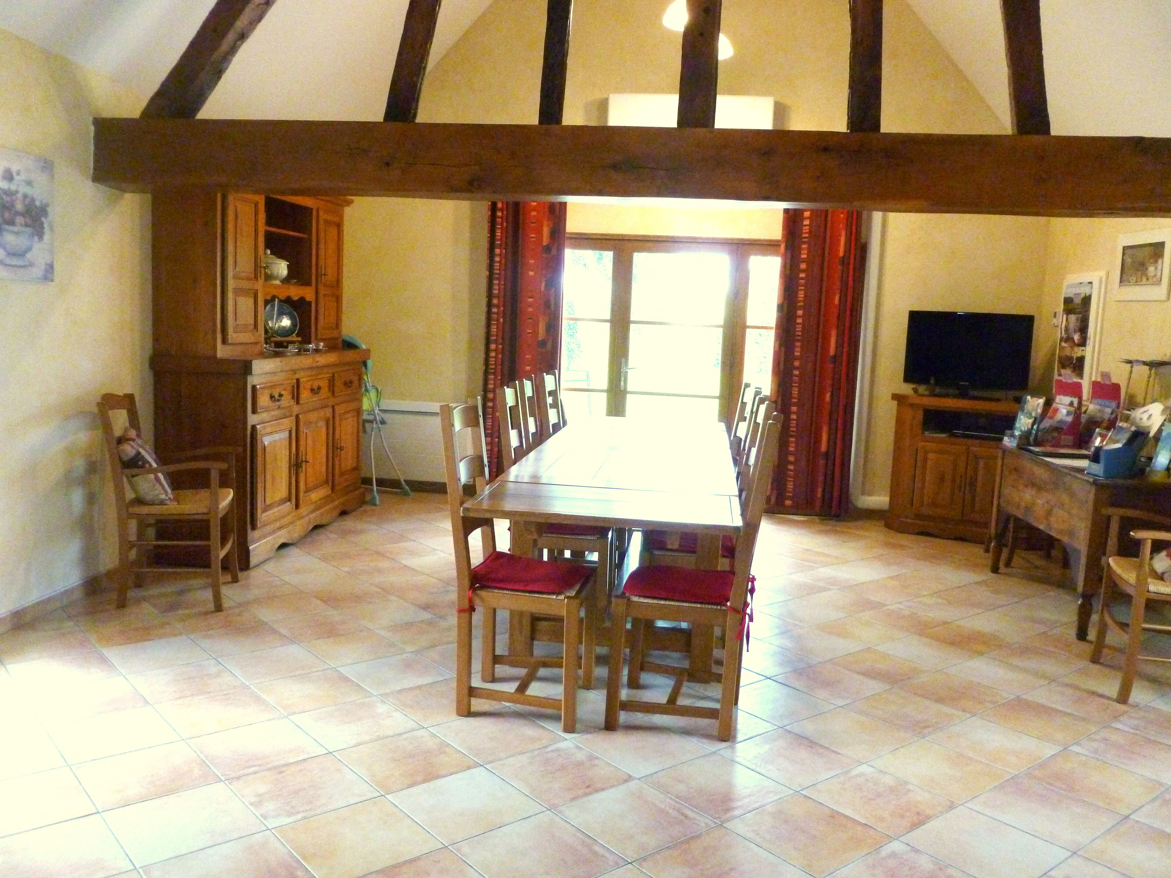A dining area with a wooden table and chairs, a kitchen with wooden cabinets, and a television on a stand.