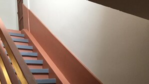 Una scala con gradini alternati di colore rosso e blu e una ringhiera in legno.