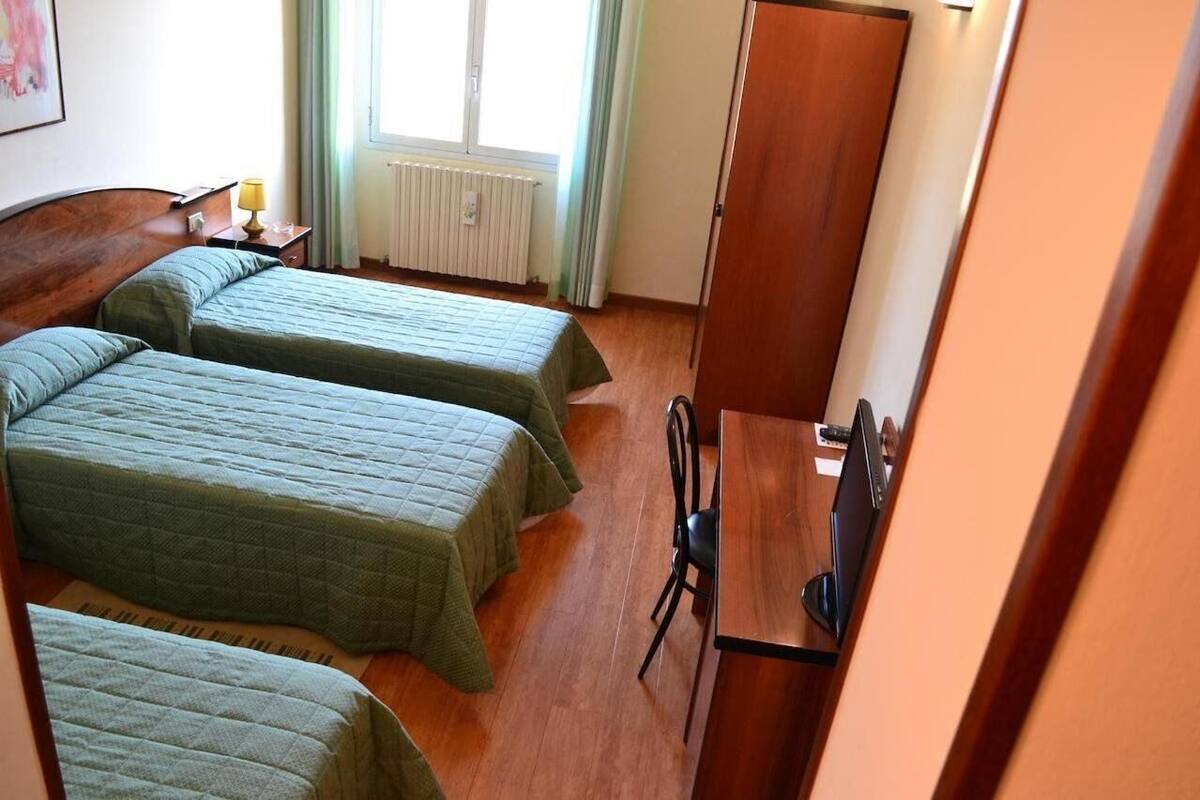 A room with two beds, a wooden desk, a chair, and a radiator.