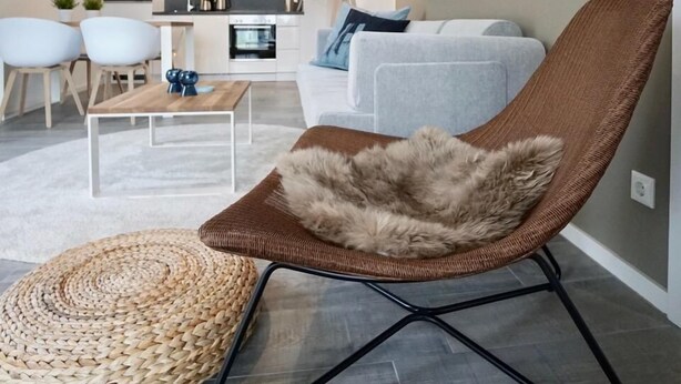 Ein modernes Wohnzimmer mit einem braunen Gewebesessel, einem runden Webteppich und einem grauen Sofa.