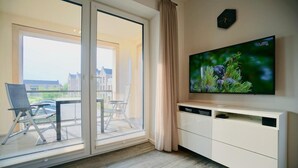 Ein modernes Wohnzimmer mit einer Schiebeglastür, die auf einen Balkon führt, einem Wand-Fernseher und einer schlichten, weißen Unterhaltungseinrichtung.