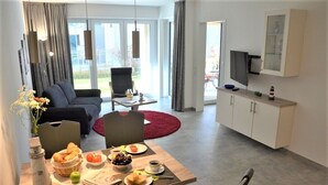 A modern living room with a dining table set for breakfast, a sofa, and a TV mounted on the wall. - Hello and welcome to the "Lighthouse" (Dangast)