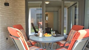 A glass-enclosed patio with a round table and four orange chairs. - Hello and welcome to the "Lighthouse" (Dangast)