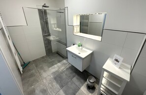 Ein modernes Badezimmer mit einer gläsernen Duschkabine, einem weißen Waschbecken und einem Spiegel darüber.