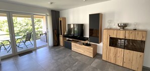 Ein modernes Wohnzimmer mit Fernseher, Holzschränken und einer Schiebeglastür, die zu einem Außenbereich führt.