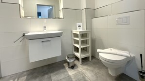 Een moderne badkamer met een wit wastafelmeubel, een spiegel met verlichting, een toilet en een klein wandrek.