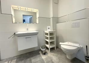 Une salle de bain moderne avec un meuble-lavabo blanc, un miroir avec éclairage intégré, des toilettes et une poubelle.