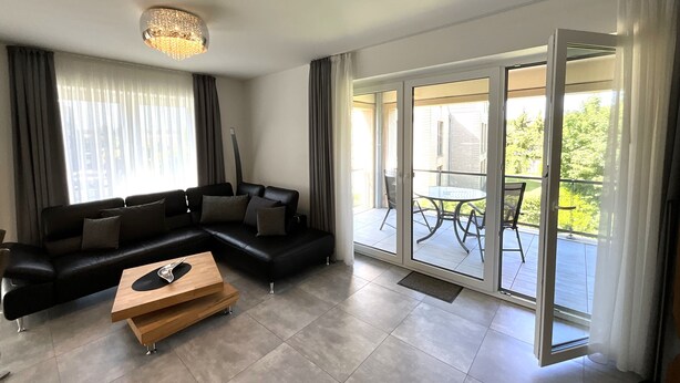 Een moderne woonkamer met een zwarte bank, een houten salontafel en een grote glazen schuindeur die leidt naar een buitenpatio.