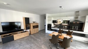 Een moderne keuken met een eethoek, geïntegreerde apparatuur en een grote flatscreen-tv.