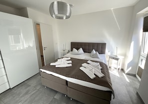 Une chambre à coucher moderne avec un grand lit, des tables de chevet, une armoire et un luminaire suspendu.