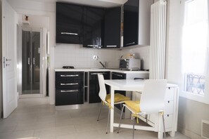 Cozinha moderna com armários pretos, bancada branca e área de refeições com mesa e cadeiras brancas.