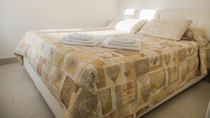 Een net opgemaakt bed met een gewatteerde sprei en twee opgevouwen handdoeken aan de zijkant.
