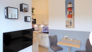 A modern room with a flat-screen TV, a small table with chairs, and a painting of a lighthouse on the wall.