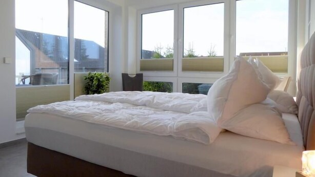A bedroom with a large bed, multiple windows, and a view of the outside.